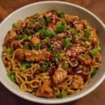 Noodles glistening in sauce with chunks of sticky garlic chicken